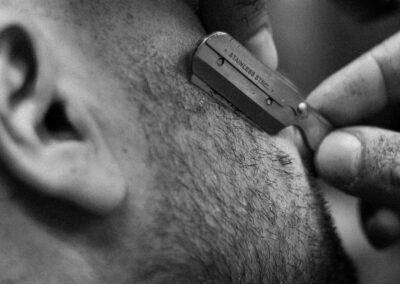 Detailed black and white image of a man shaving with a straight razor, showing texture and technique.