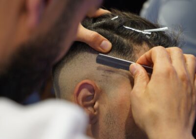 Close-up of a barber giving a modern haircut with a straight razor in a salon.