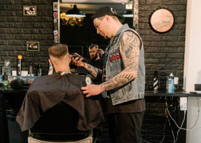 A tattooed barber skillfully trims a client's hair in a stylish barber shop.