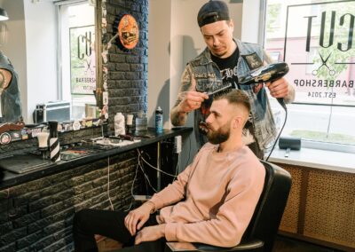 Barber styling a man's hair with a blow dryer in a contemporary barbershop setting.