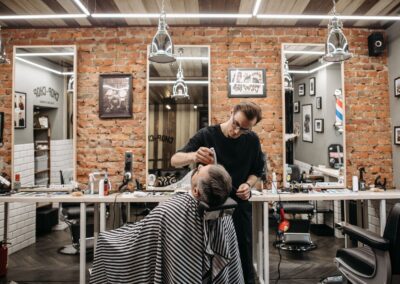 Barber working on a client's haircut in a stylish barbershop with brick walls and mirrors.