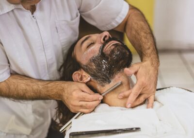 A professional barber skillfully shaving a client's beard with a straight razor in a barbershop setting.
